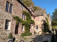 Colour photo of the exterior of Cromford Bridge House, a fairly large, pretty cottage with climbing plants.