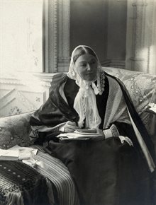 Black and white photograph of an elderly Nightingale sitting in her London home, holding documents.