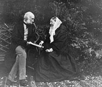 Photograph of an elderly Nightingale with Sir Harry Verney in the gardens of Claydon house. They sit facing each other on a bench, Nightingale is wearing a black dress and white shawl.