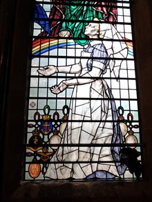 Glass image of a nurse in a blue and white dress looking upwards. In the background is a rainbow and Christian imagery. imagery.